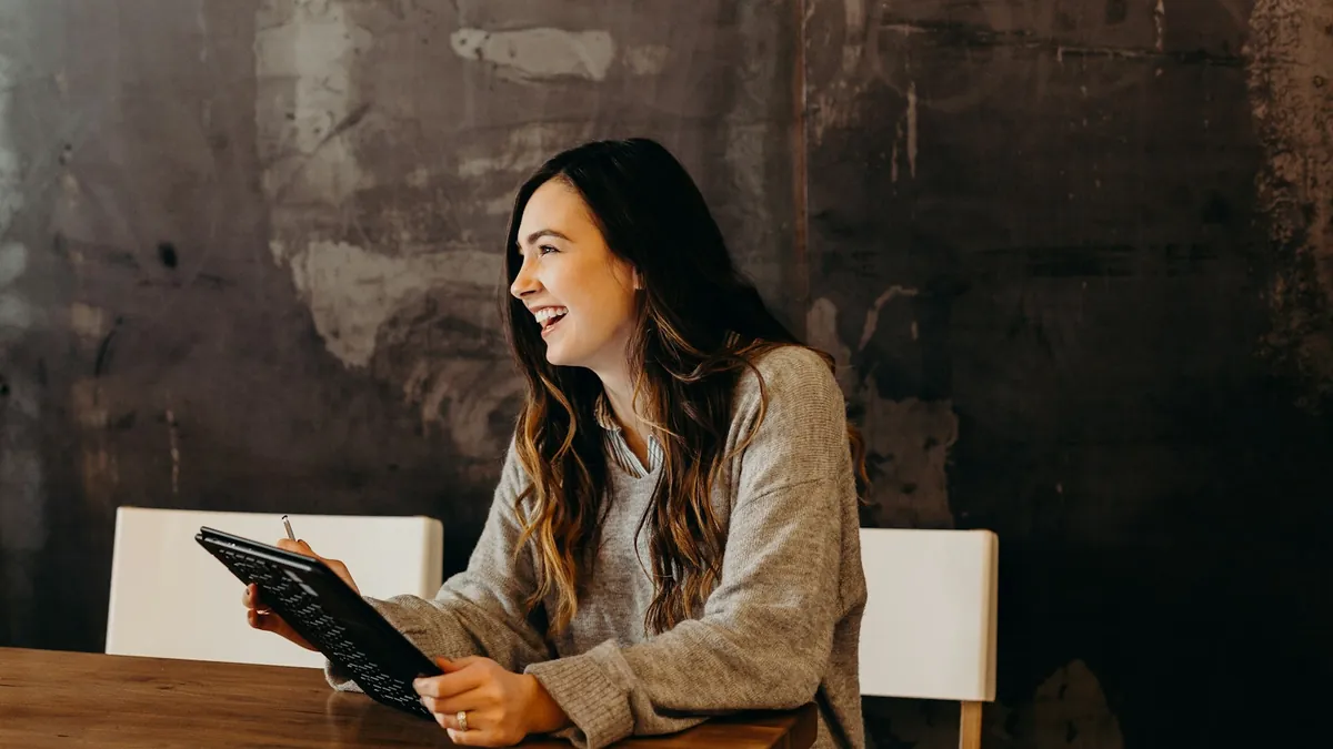 Dona de cafeteria sorridente usa uma tablet com teclado anexado na mesa do salão do restaurante
